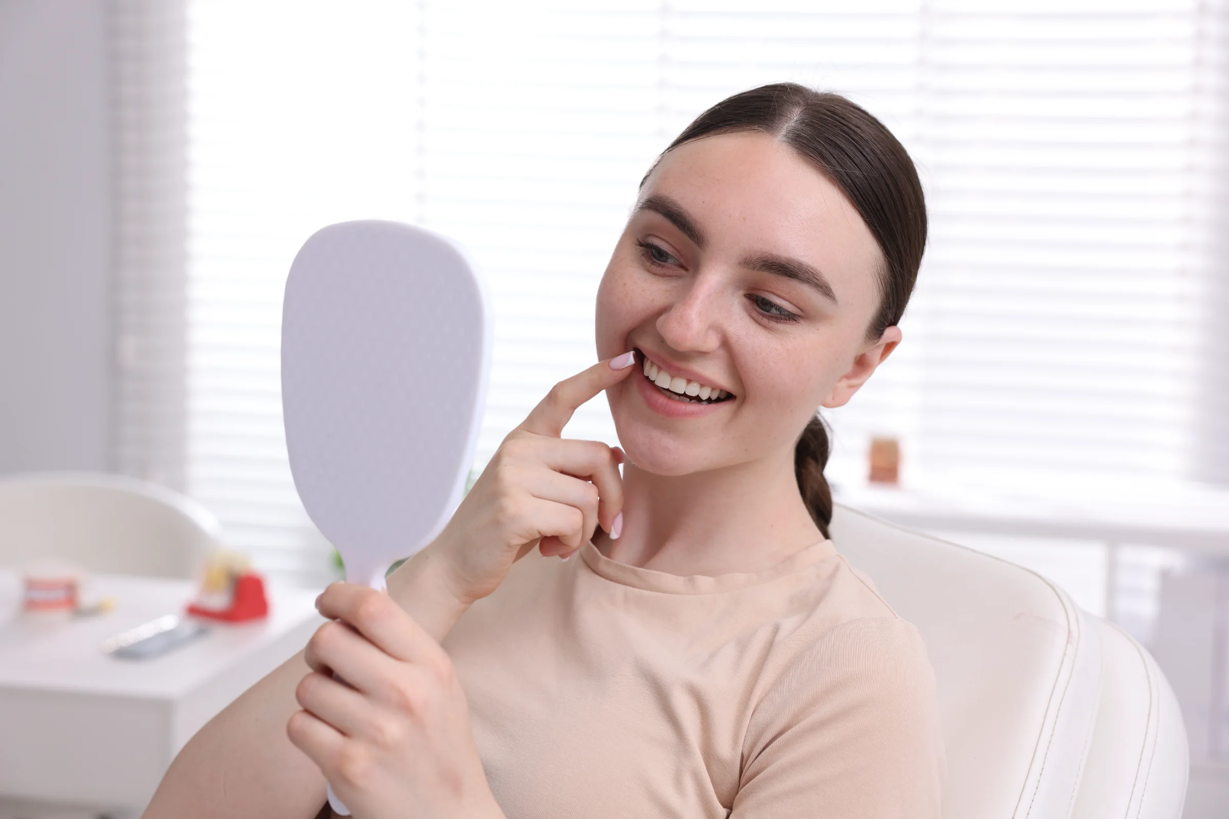 Smiling woman checking her whiter teeth in a hand mirror