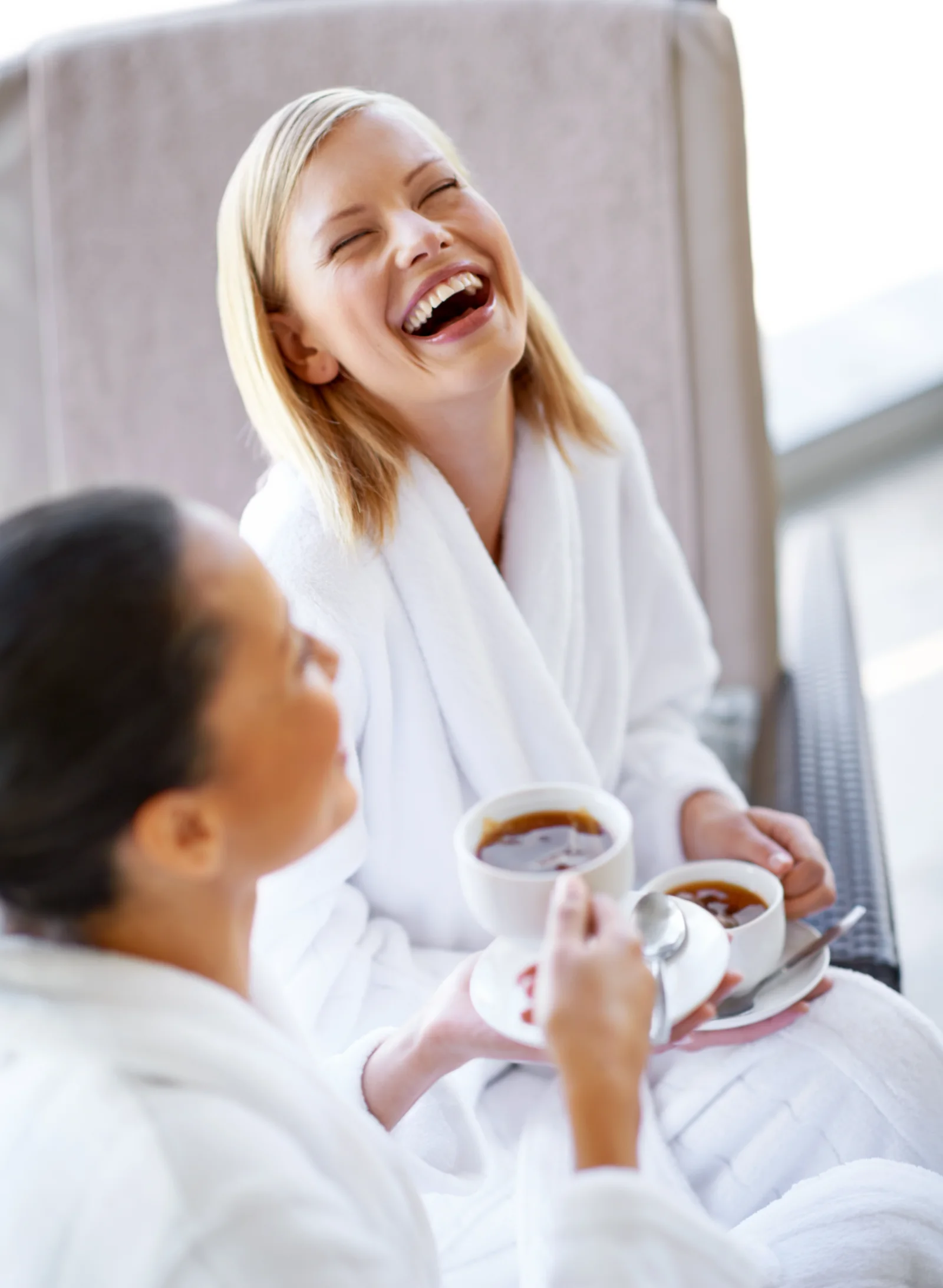 Two friends in white robes laughing together at a spa